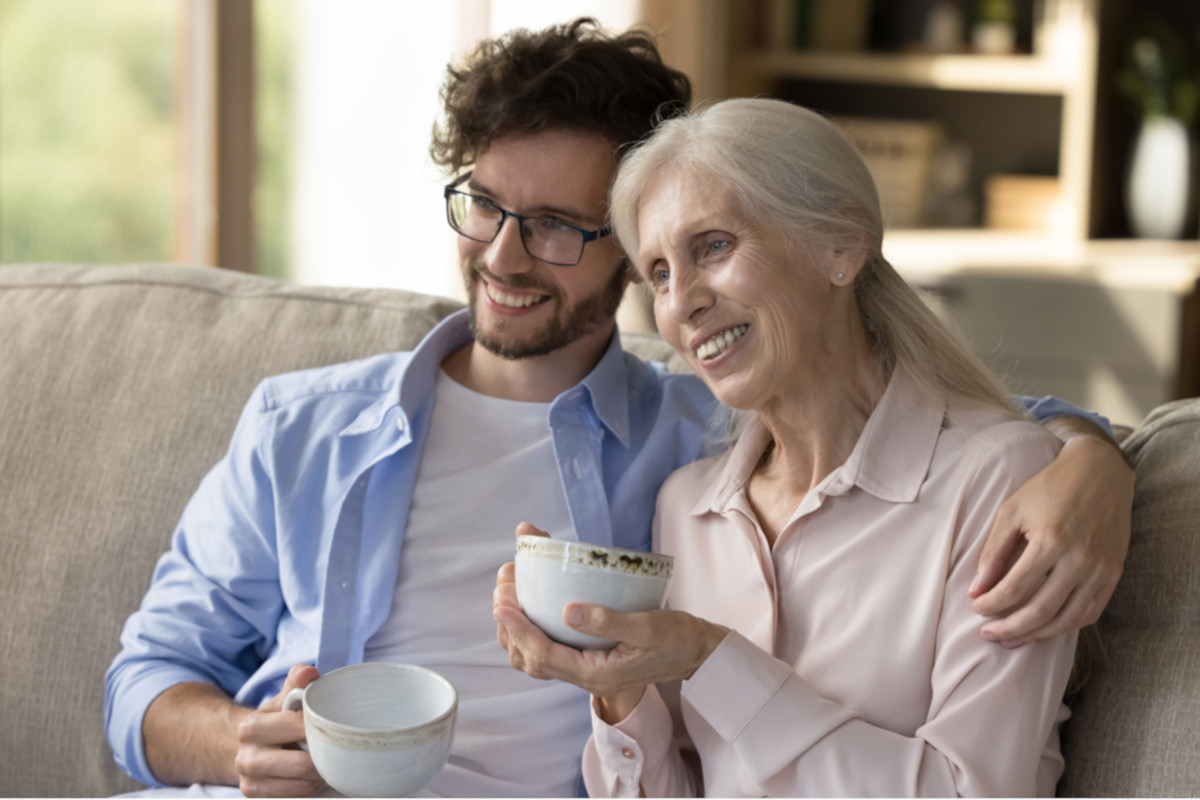 An adult child and their older parent sharing a cup of tea and a laugh together.